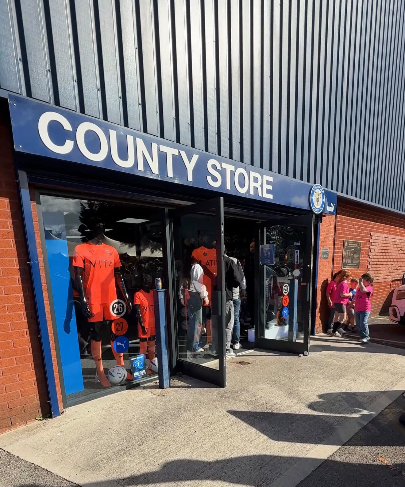 The club shop with its County Store sign on the stadium’s brick wall; orange shirts in the window, supporters going in through the door